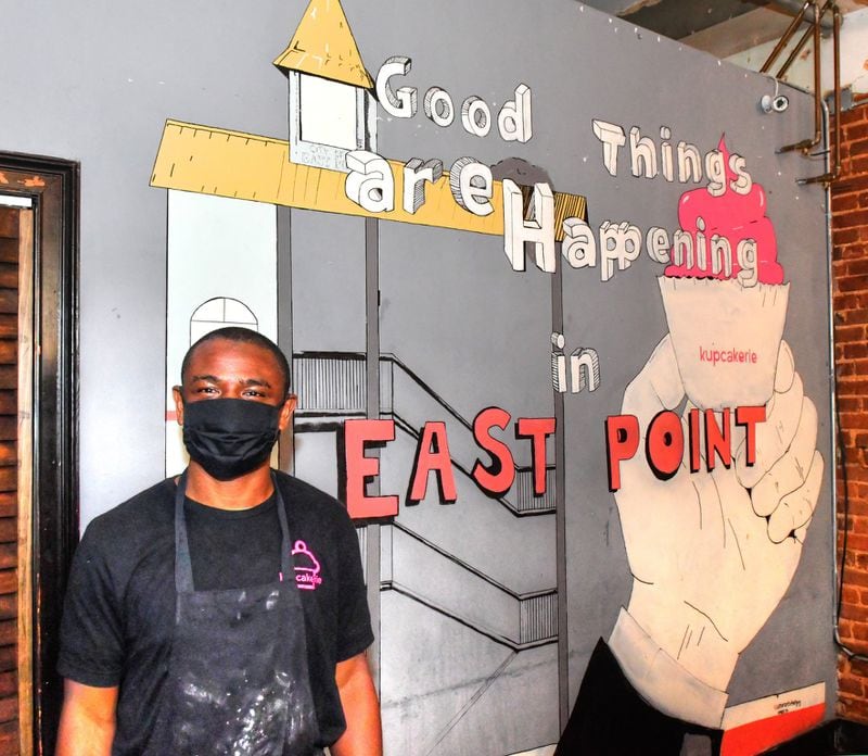 Henry Adeleye, co-owner of Kupcakerie on Main Street in East Point, stands in front of a mural in the bakery. Adeleye and his wife, Kascha, opened the brick-and-mortar space in 2016, after two years of building their cupcake business through shipping and delivery. CONTRIBUTED BY CHRIS HUNT PHOTOGRAPHY